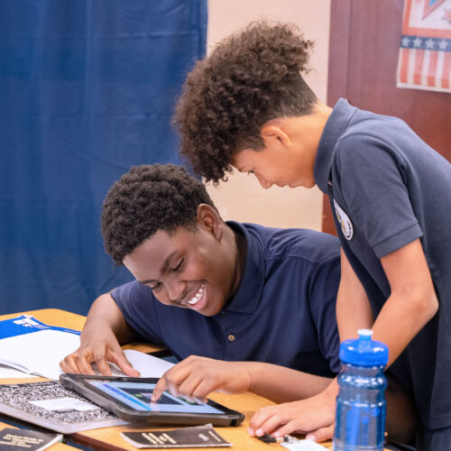 Two middle school students work together on a tablet at a desk