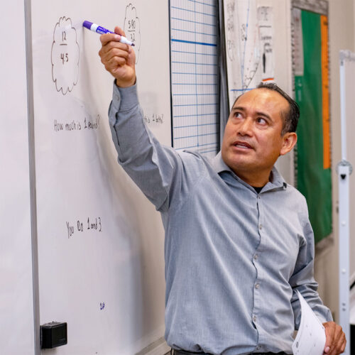 An educator points to a whiteboard with a marker in front of a classroom