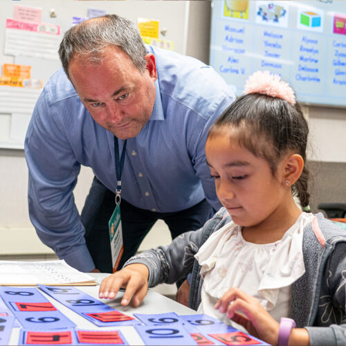 A superintendent joins a student at a table as they move numbered tiles