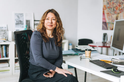 Portrait of charming smiling adult woman middle aged with curly hair architect designer manager working in bright modern office
