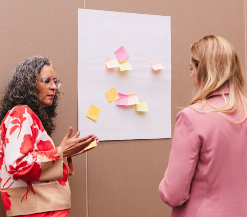 Two adults discuss in front of sticky notes on a wall