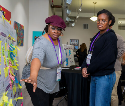 Two event attendees discuss in front of a poster with sticky notes