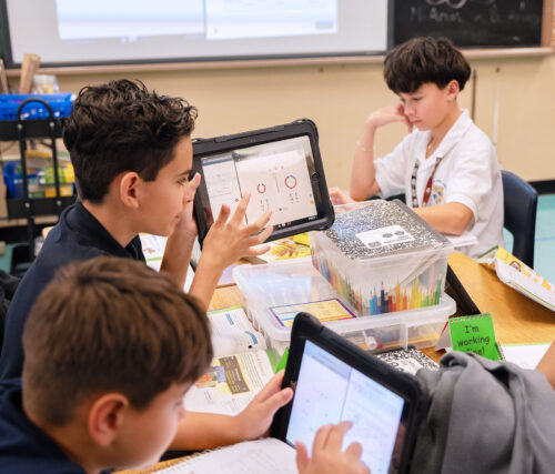 Three students work on their tablets together at a table in a classroom