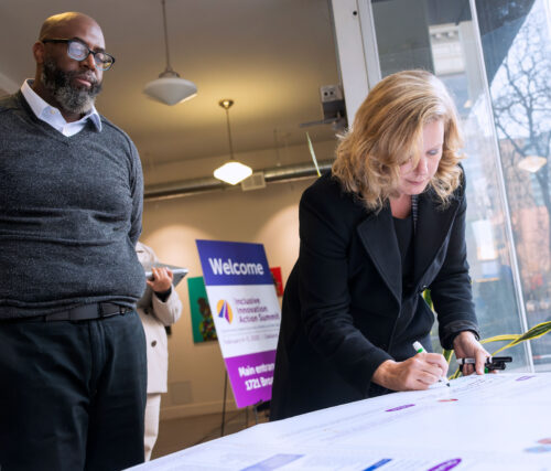 Two people gather around a table and watch as an attendee writes on a poster
