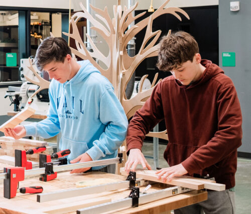 Two high school students in a workshop work on a woodworking project