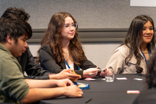 Three students sit around a table smiling.