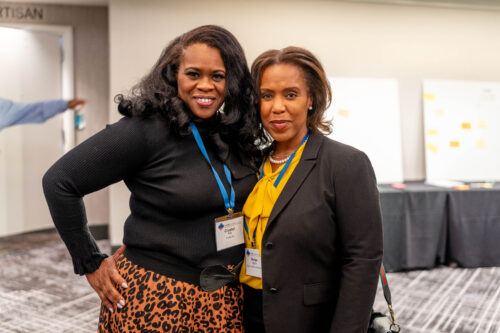 Two women smile for a photo while wearing lanyards and badges.