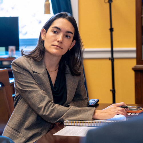 Woman in a business suit holds a pen and sits at a table with a notebook