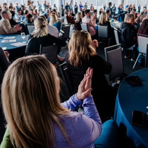 A group of people clap while seated at tables during a convening