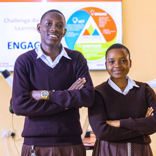 Two students stand in front of a poster with their arms crossed and smile at the camera