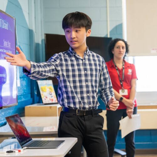 A young student points to a screen as they present in front of a classroom