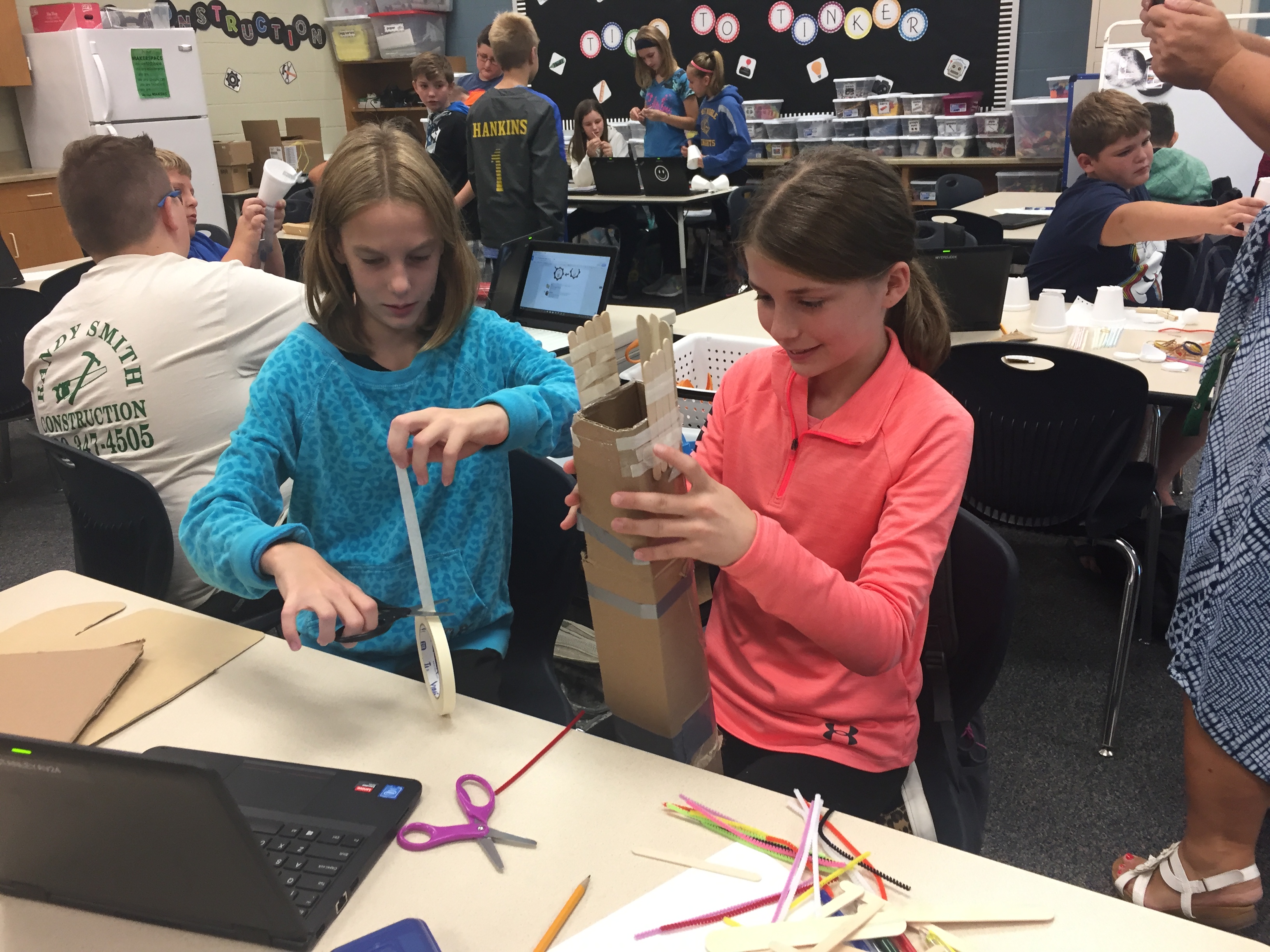 Two students tape together a project made of popsicle sticks and cardboard.