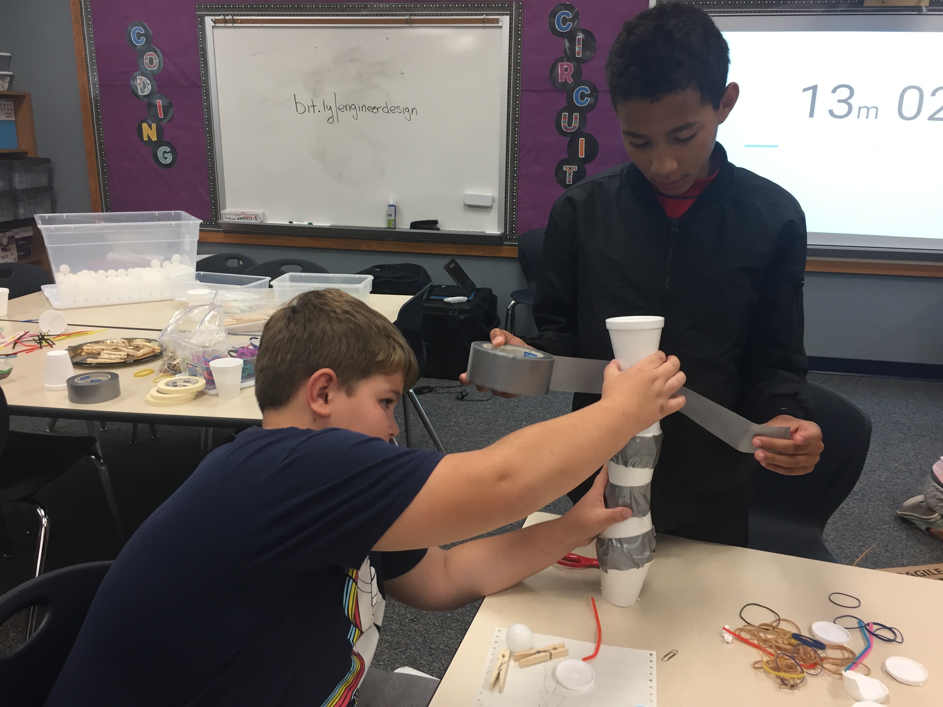 Two students tape together styrofoam cups.