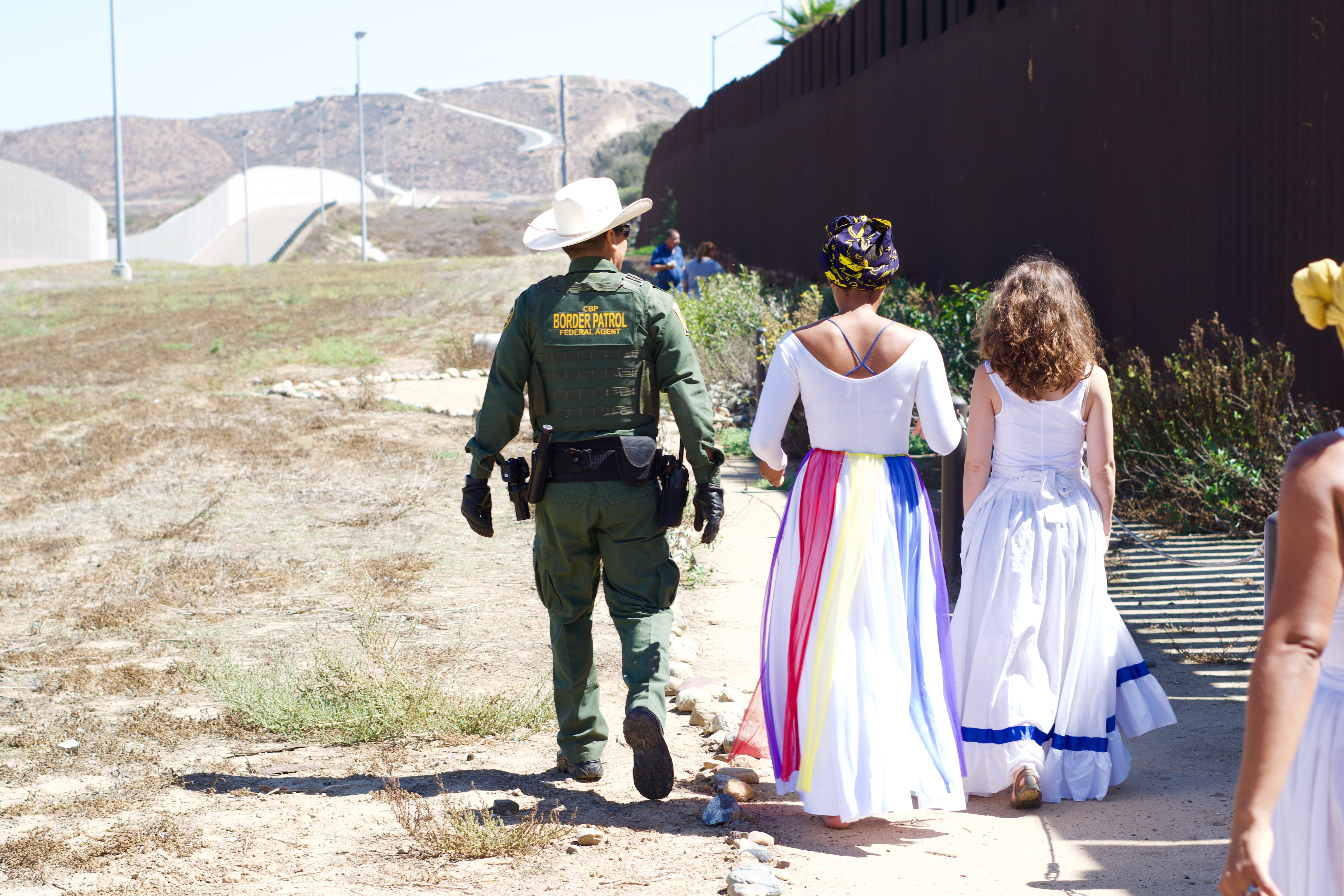 A border patrol agent walks next to a group of dancers at Friendship Park