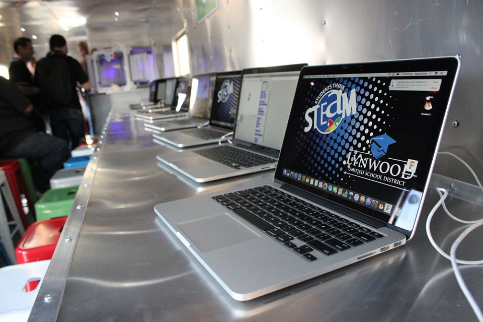Photograph of a row of laptops on a desk, with one laptop featuring a background of the Lynwood Unified School District logo