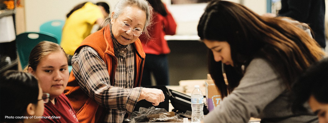 Older Asian woman facilitates project with small group of diverse students