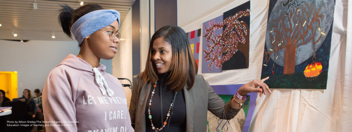 Black female teacher pleasantly discusses artwork with Black female student