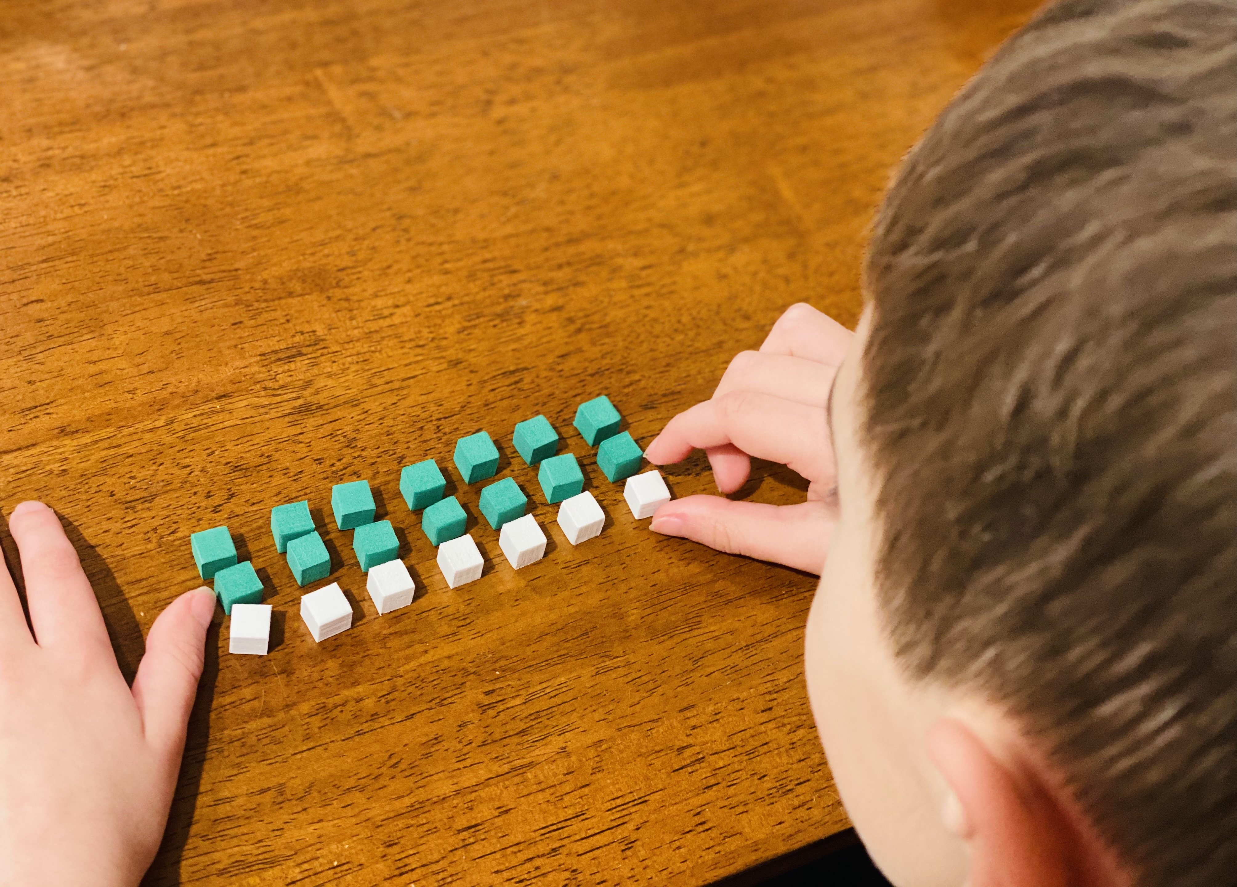 Photo of young male student using green and white foam cube manipulatives to show thinking on how to solve 7x3. 