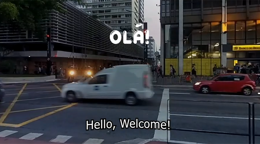 Image of street with cars passing and Olá (Hello, Welcome) written on the screen