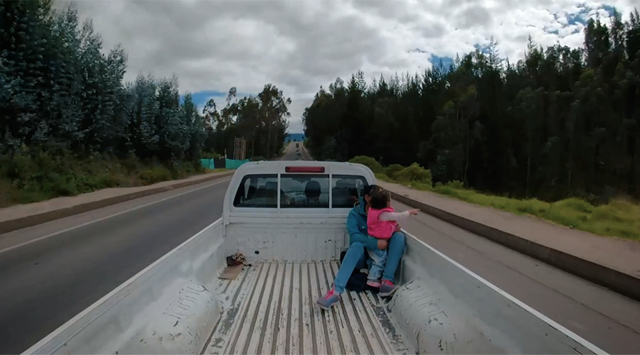Screenshot from Cruzar trailer with woman and child riding in back of a pickup truck