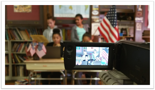 An image of a camera recording a group of students broadcasting from a classroom. 