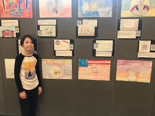 A student stands in front of a gallery of illustrations posted to a wall.