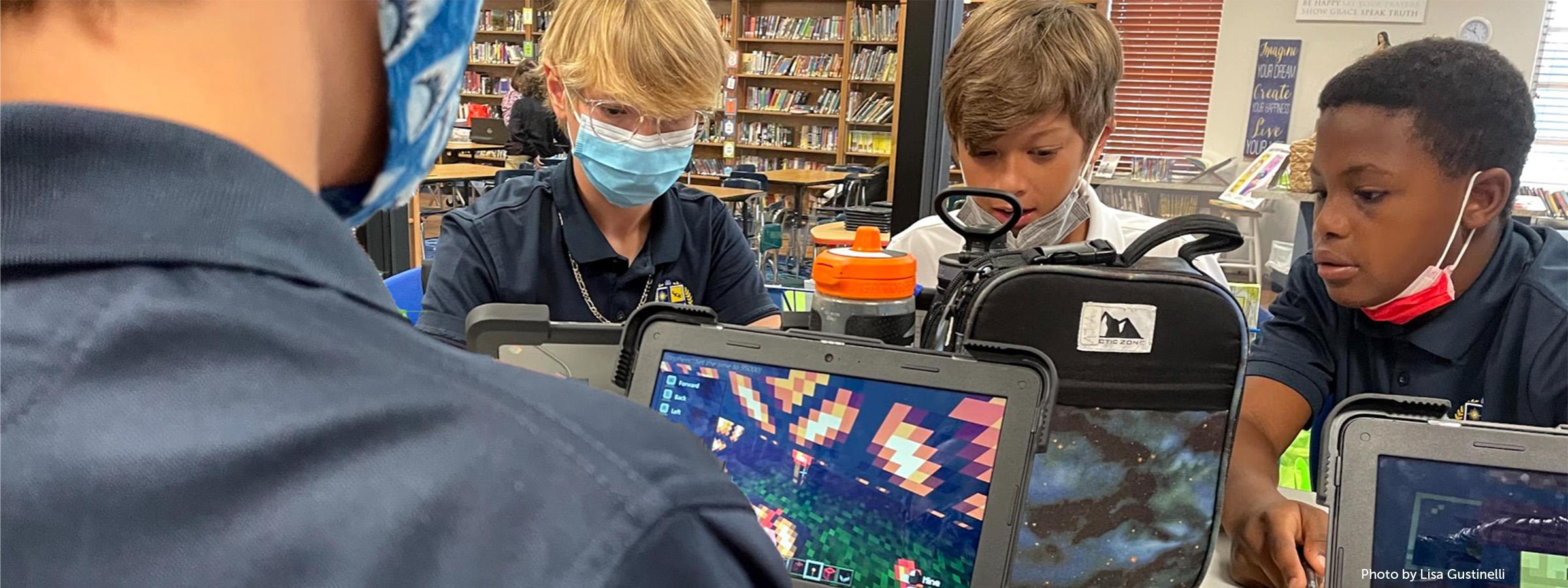 Four middle school students play minecraft on their laptops
