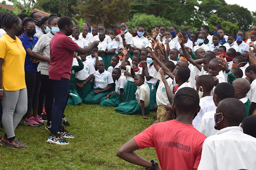 High school aged girls speaking to a large group of primary school students outside. 