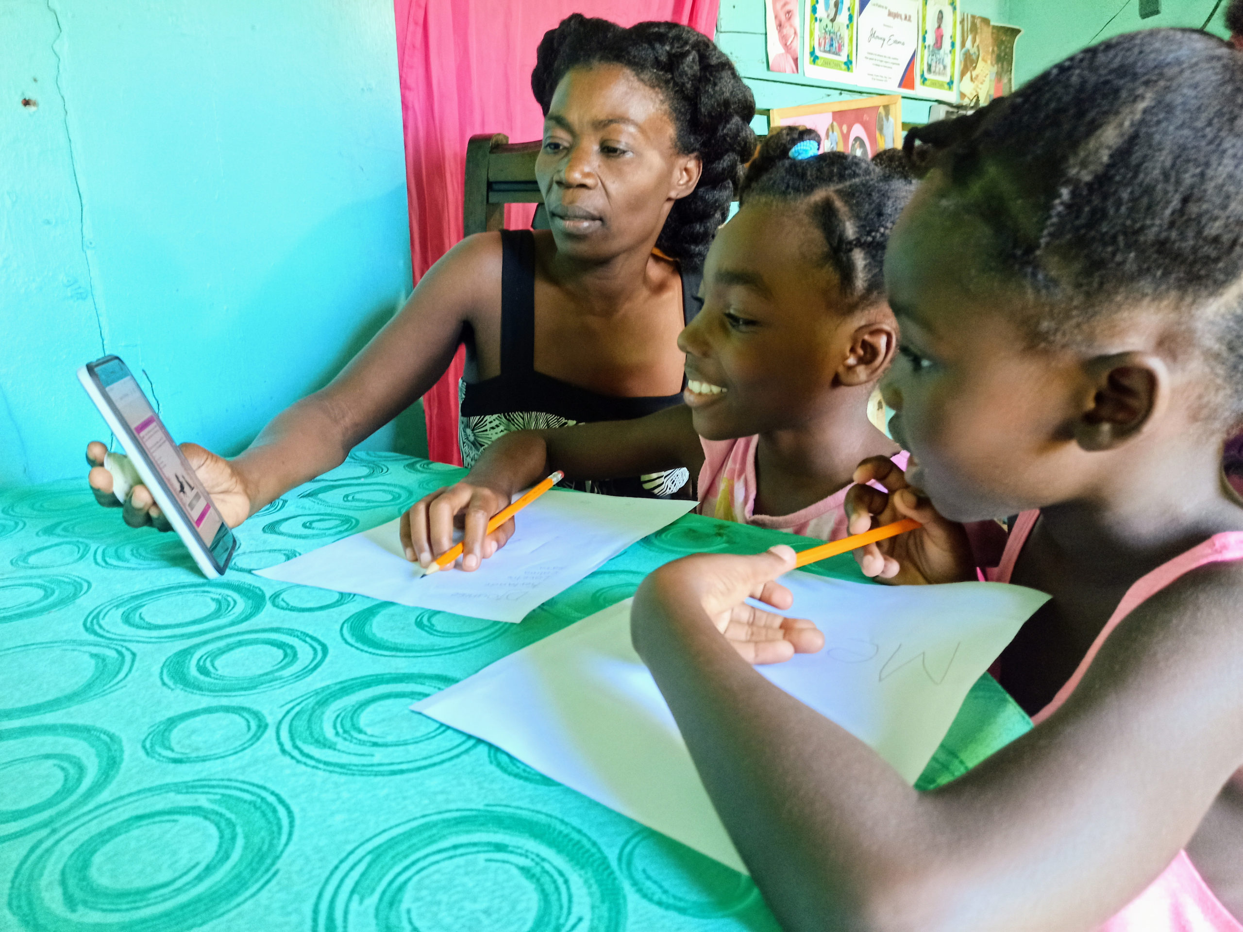 A Haitian mother and her daughters work together on Blue Butterfly's distance learning program on a tablet