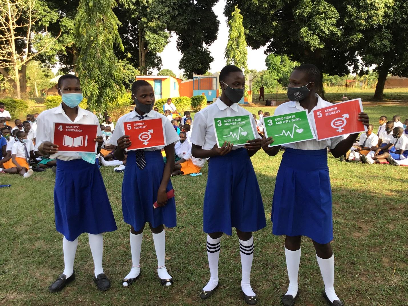 Alt text: Four girls holding Sustainable Development Goal posters: Quality Education, Gender Equality, and Good Health and Well Being.