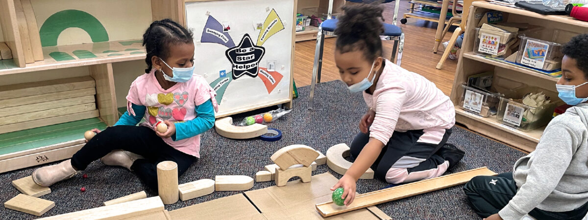 three preschool aged children play with blocks, while wearing masks