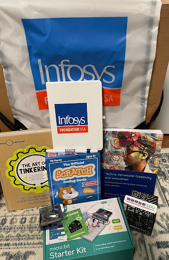 Infosys Foundation USA gift bag contents displayed with the books The Art of Tinkering and Techno-Vernacular Creativity, a set of boxed Scratch coding cards, a micro:bit circuit set with a boxed starter kit, a Merge Cube from Merge Edu and Infosys Foundation USA journals and pens.