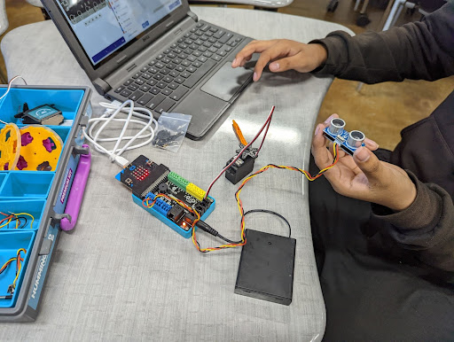 Image shows students working on laptops connected to micro:bit electronics circuitry sets. 