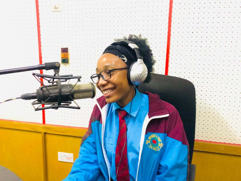 A student has on headphones and sits in front of the microphone at a radio station