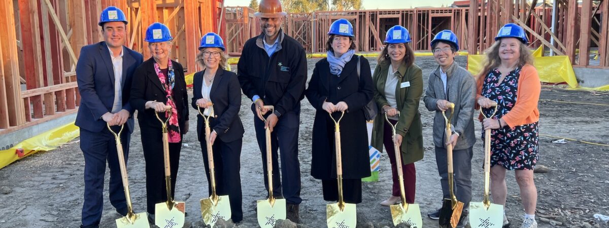 A group of adults with hard hats and gold shovels pose for a photo at the groundbreaking for Mountain View Whisman School District's affordable staff and teacher housing project.