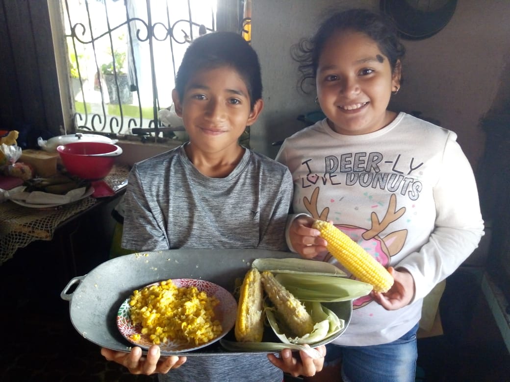 Two children smile as they present a platter of food