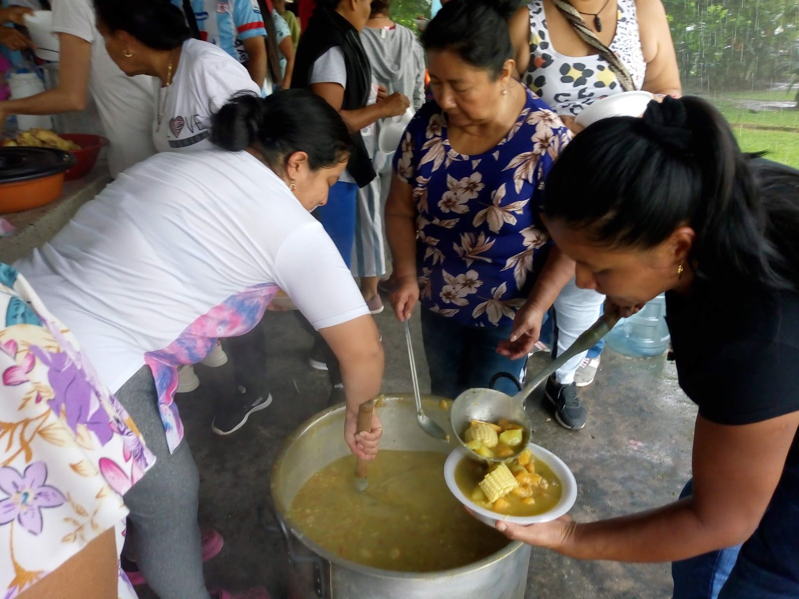 A group of adults scoop food out of a large pot 