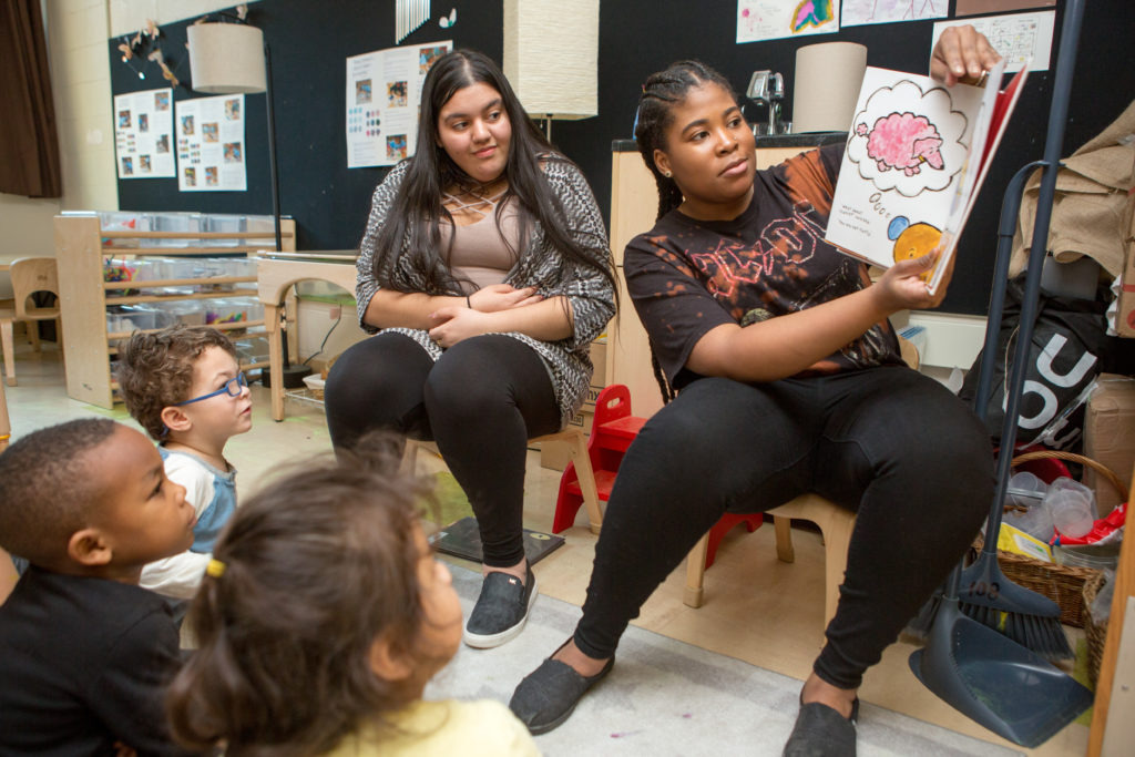 Two high school students reading a book aloud to elementary students.