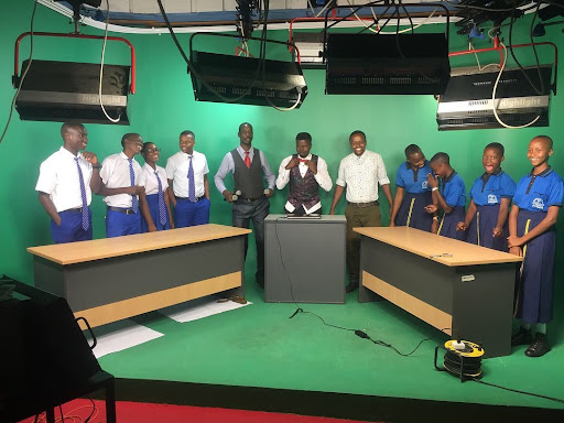 Mahamba Sebastian and his students pose in front of a green screen in a TV recording studio. 