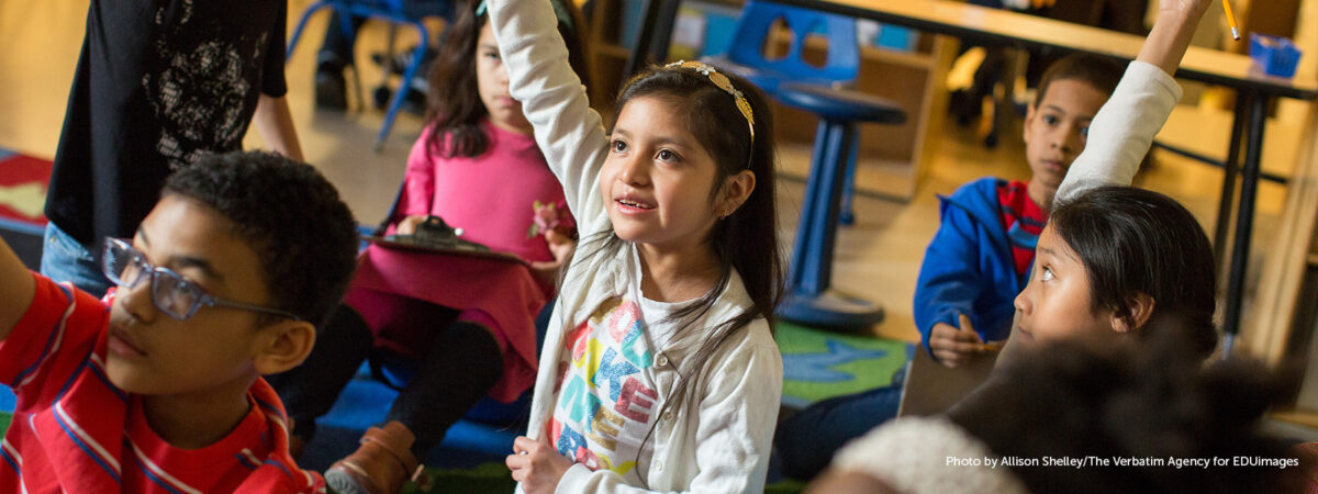 A third grader raises her hand to answer a teacher’s question during a math lesson.