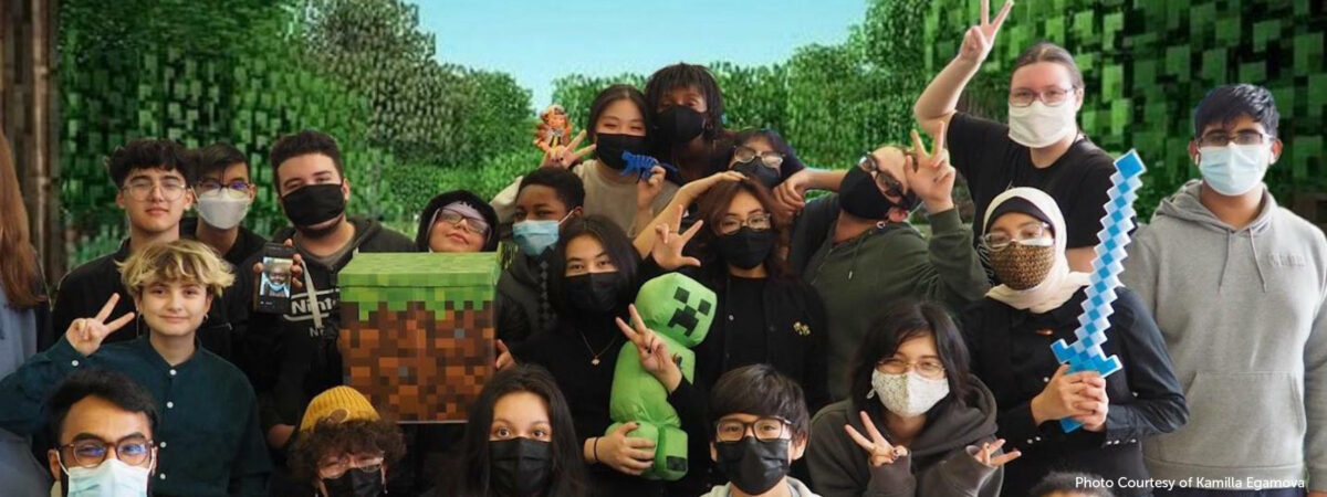 A group of students stand in front of a minecraft background while holding minecraft-themed props.