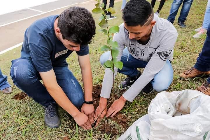 Two students place a plant in the ground. 