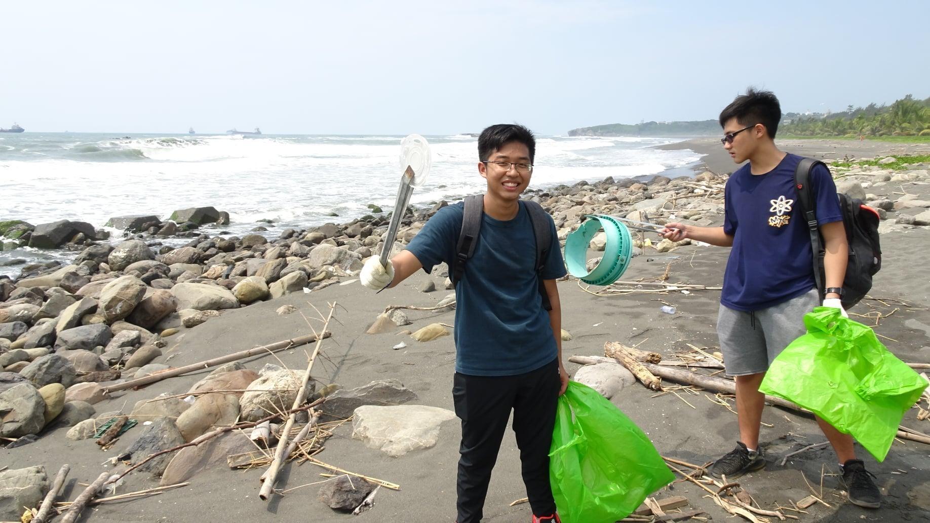 Two students collect trash on the beach.