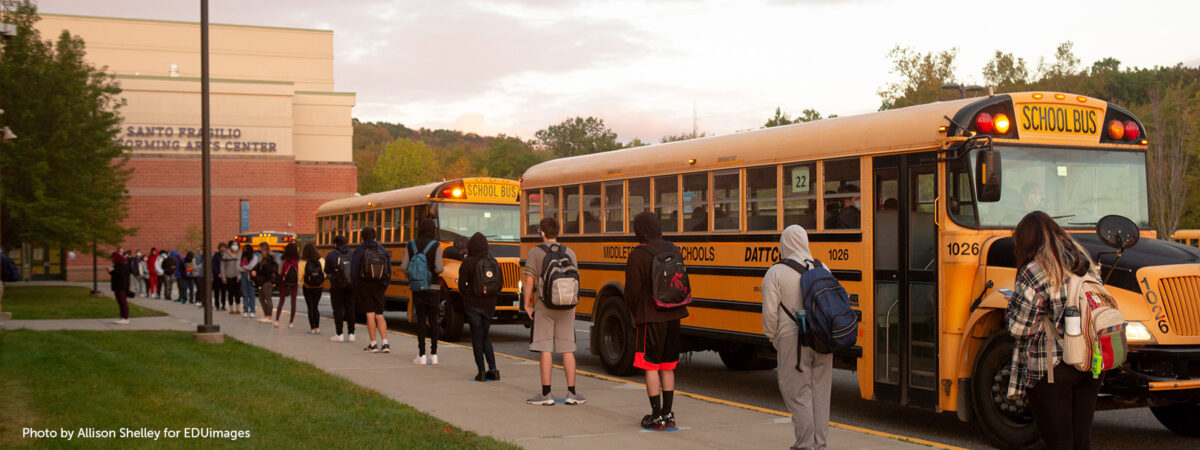 An image of students lined up in front of a bus, while standing six feet apart