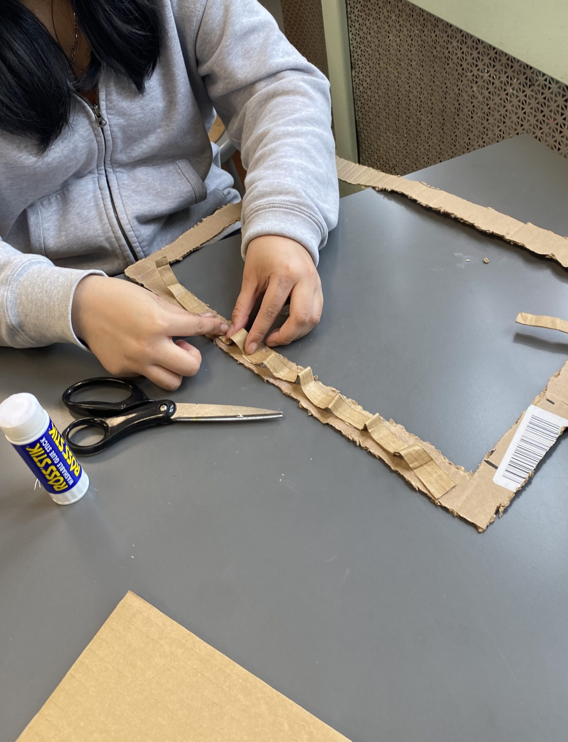 A student’s hands craft a cardboard frame. 