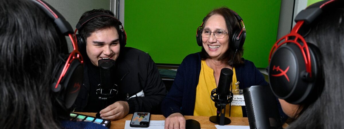 Group of individuals sitting down with headphones on and a microphone in front of one woman.