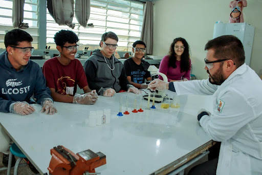 A teacher demonstrates an experiment to students at a lab desk. 