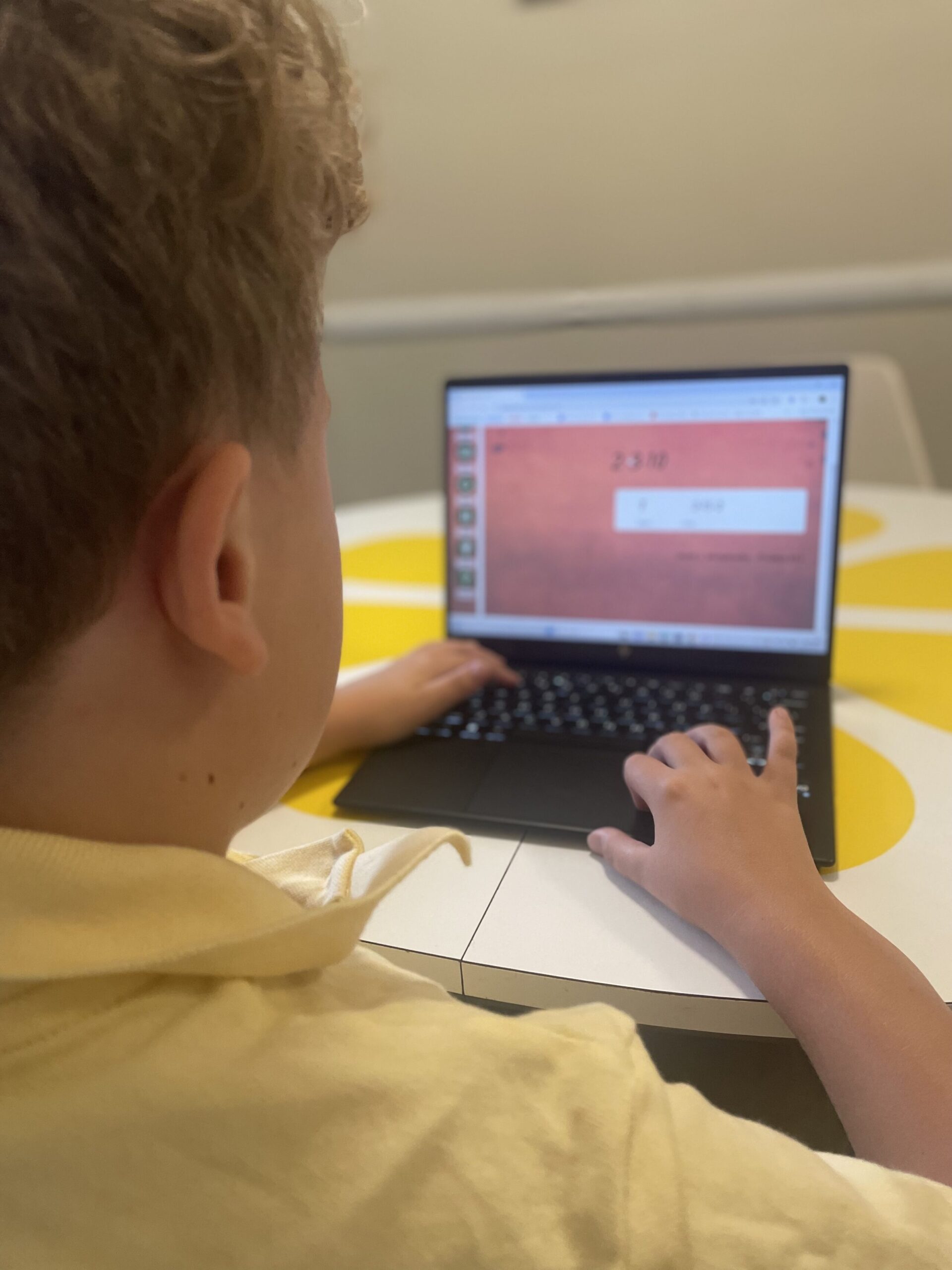 Child seated at white and yellow table in front of laptop