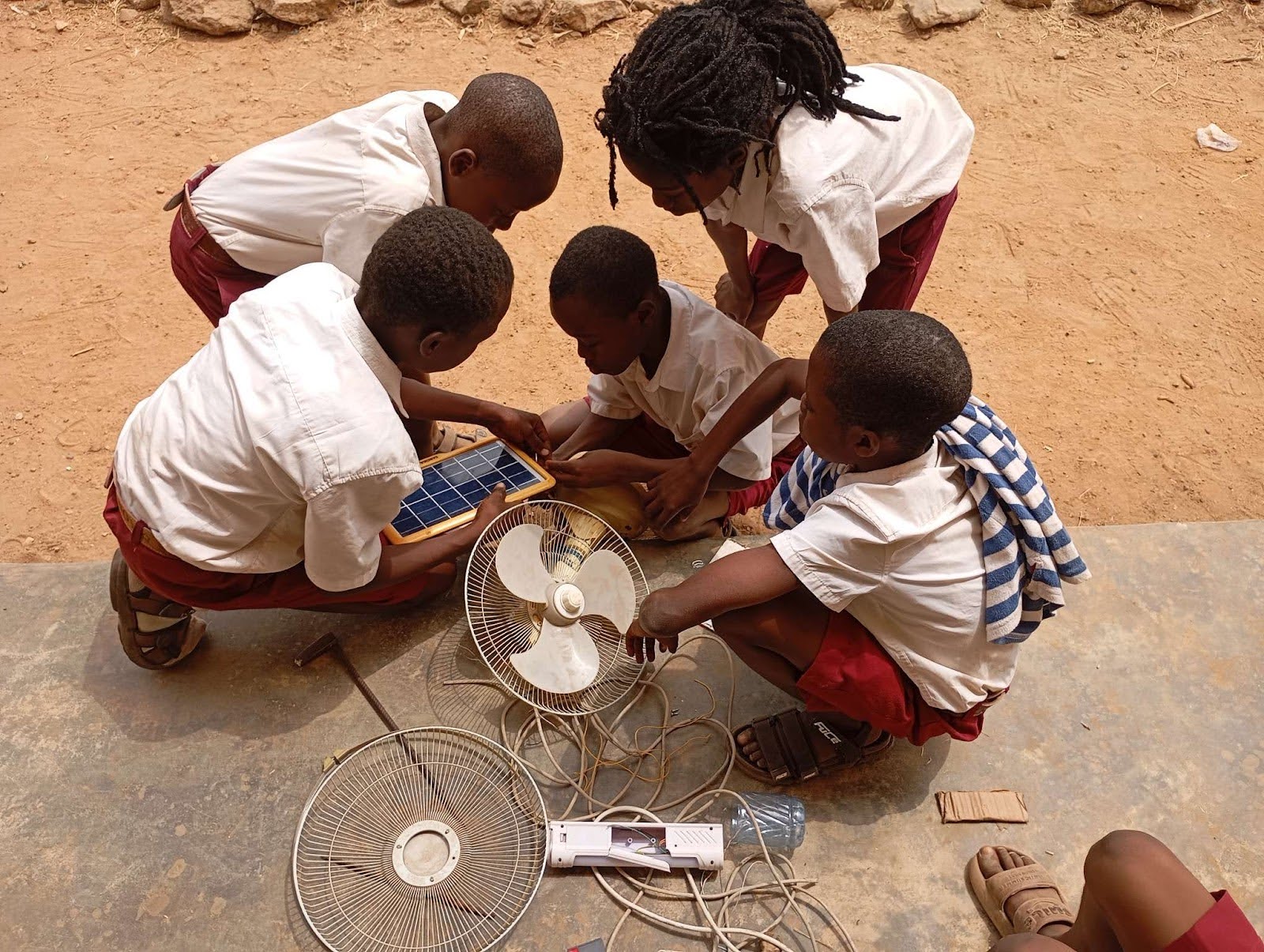 A group of students huddle around a solar panel and fan.