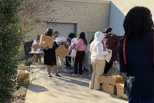 Students and community members assemble outside of their school with boxes and other materials. 